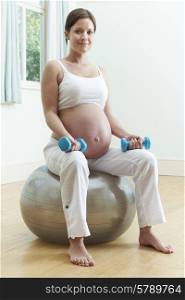 Pregnant Woman Sitting On Exercise Ball With Weights