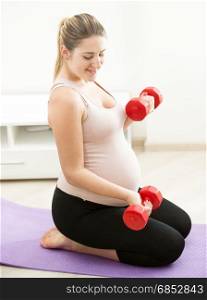 Pregnant woman sitting on fitness mat and exercising with weights