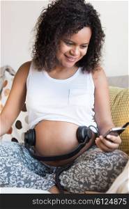 Pregnant woman sitting on sofa and listening music in headphones