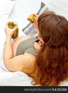 Pregnant woman sitting on sofa at home and holding jar of cucumbers in hands. Closeup.&#xA;