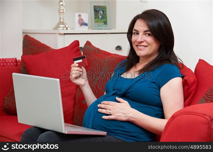 Pregnant Woman Sitting On Sofa Using Credit Card To Shop Online