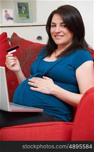 Pregnant Woman Sitting On Sofa Using Credit Card To Shop Online