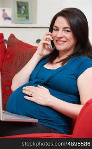 Pregnant Woman Sitting On Sofa Using Laptop And Mobile Phone