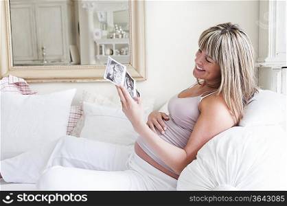Pregnant woman sitting on sofa with baby scan photos
