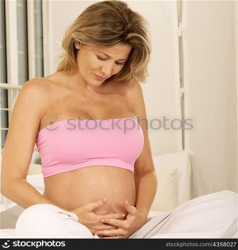 Pregnant woman sitting on the bed touching her abdomen