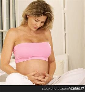 Pregnant woman sitting on the bed touching her abdomen