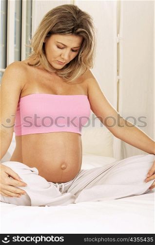 Pregnant woman sitting on the bed with her hands on her knees