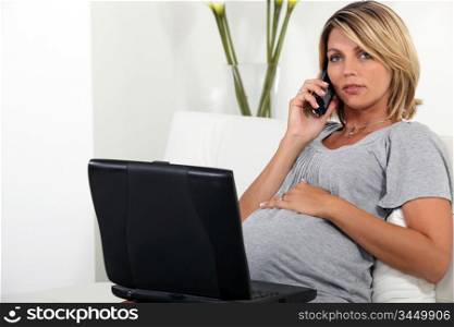 Pregnant woman sitting on the sofa with a laptop and telephone