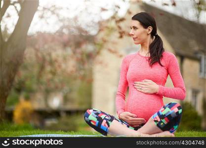 Pregnant woman sitting outdoors, holding belly