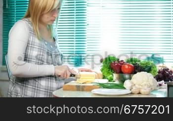 pregnant woman slicing the cheese on the kitchen table