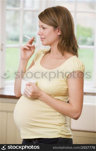 Pregnant woman standing in kitchen with coffee and cigarette