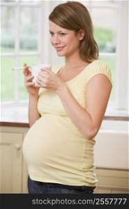 Pregnant woman standing in kitchen with coffee and cigarette smiling