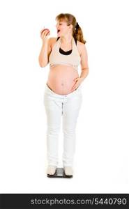 Pregnant woman standing on weight scale and eating apple isolated on white&#xA;