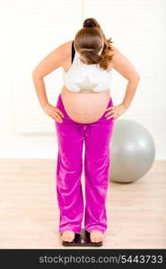 Pregnant woman standing on weight scale at living room&#xA;