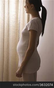Pregnant woman stands at window with closed curtains