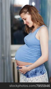 Pregnant woman stands in the room with her hands on belly