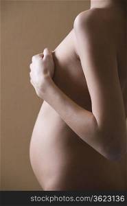 Pregnant woman stands with hand covering naked breast