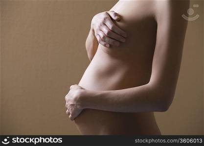 Pregnant woman stands with hand covering naked breast and stomach