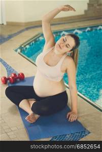 Pregnant woman stretching on fitness mat at swimming pool