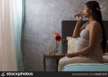 Pregnant woman talking medicine while sitting on bed at home