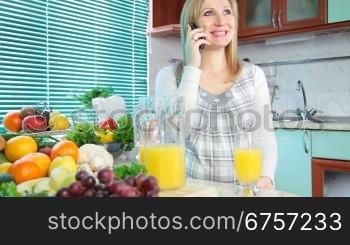 Pregnant woman talking on her mobile phone and drink orange juice in the kitchen