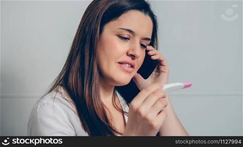 Pregnant woman talking on mobile phone looking positive pregnancy test