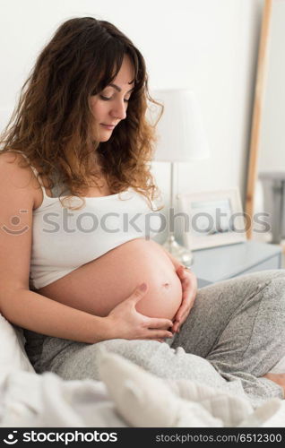 Pregnant woman touching her belly. Happy pregnant woman sitting and touching her belly at home