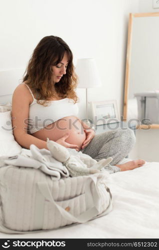 Pregnant woman touching her belly. Happy pregnant woman sitting and touching her belly at home