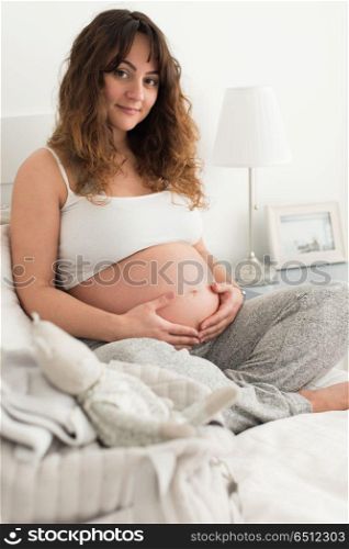 Pregnant woman touching her belly. Happy pregnant woman sitting and touching her belly at home