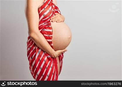 Pregnant woman touching her tummy standing over plain background. Pregnancy, expectation, motherhood concept