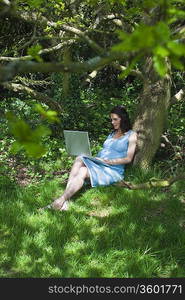 Pregnant woman using laptop in woods