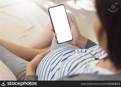 Pregnant woman using smartphone and doing online shopping on sofa. Asian Female enjoying making online video call with mobile phone during her pregnancy.