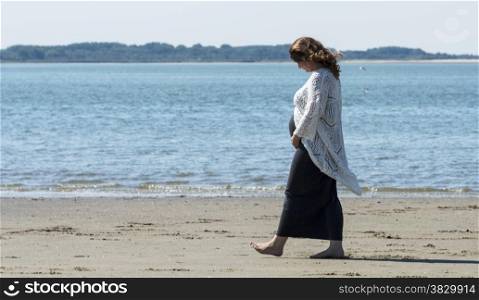 pregnant woman walking on the beach with teh sea as background