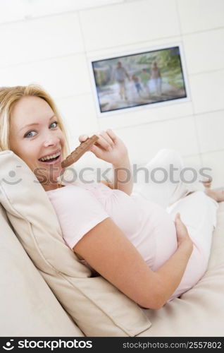 Pregnant woman watching television and eating chocolate smiling