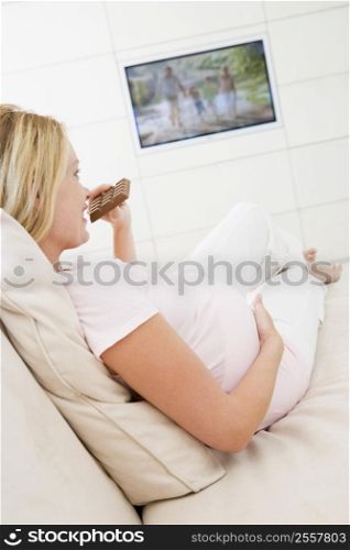Pregnant woman watching television and eating chocolate smiling