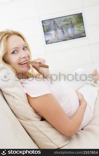 Pregnant woman watching television and eating chocolate smiling