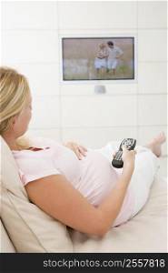Pregnant woman watching television using remote control
