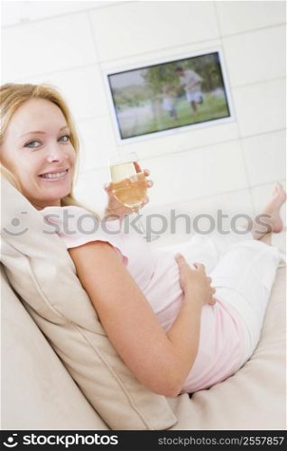 Pregnant woman watching television with glass of white wine smiling