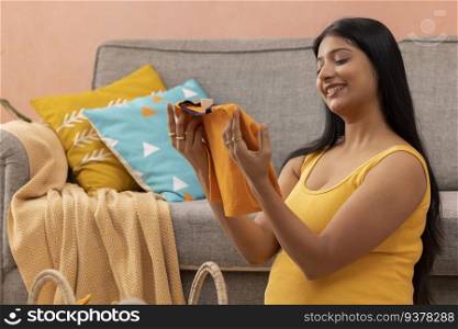 Pregnant woman watching the first clothes for her still unborn baby