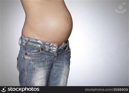 Pregnant woman wearing jeans, mid section, studio shot