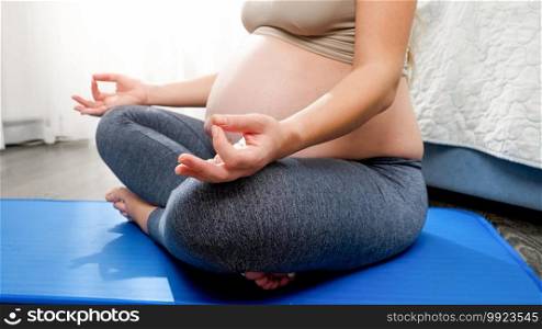 Pregnant woman with big belly meditatng while sitting in lotus pose on fitness mat at home. Concept of healthy lifestyle, healthcare and sports during pregnancy.. Pregnant woman with big belly meditatng while sitting in lotus pose on fitness mat at home. Concept of healthy lifestyle, healthcare and sports during pregnancy