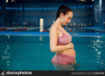 Pregnant woman with big belly swimming in the pool indoors. Pregnancy being, relaxation in the water, recreational exercise for health care. Pregnant woman with big belly swimming in the pool