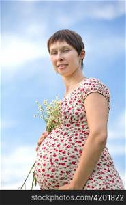 Pregnant woman with chamomile bouquet on sky background