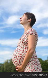 Pregnant woman with closed eyes on blue sky background