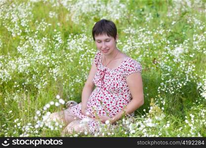 Pregnant woman with closed eyes sitting in chamomile background