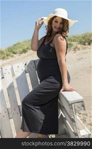 pregnant woman with hat on wooden chair on the beach