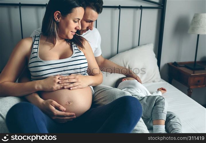 Pregnant woman with her husband looking at their sleeping son. Pregnant with her husband looking son