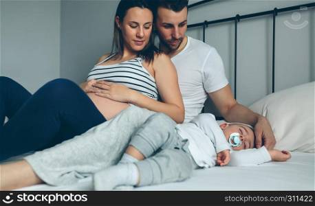 Pregnant woman with her husband looking at their sleeping son. Pregnant with her husband looking son