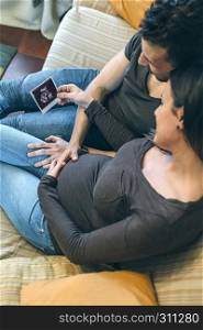 Pregnant woman with her partner looking at the ultrasound of their baby in the living room. Pregnant with her partner looking ultrasound of their baby