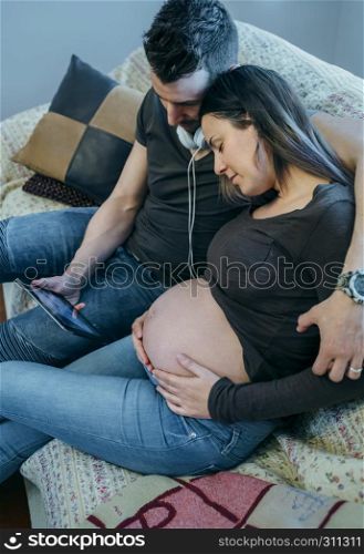 Pregnant woman with her partner looking in the tablet a ultrasound of their baby in the living room. Pregnant with her partner looking ultrasound of their baby